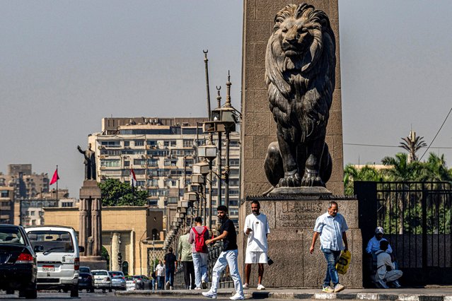 People walk past one of the four bronze lion statues at the end of the landmark Qasr el-Nile bridge connecting Cairo's central Tahrir Square to the island of Zamalek (background) on October 6, 2025. Delegations from Hamas, Israel and the United States are due to convene in Egypt for talks on October 6, with President Donald Trump urging negotiators to “move fast” to end the nearly two-year war in Gaza. (Photo by Khaled Desouki/AFP Photo)