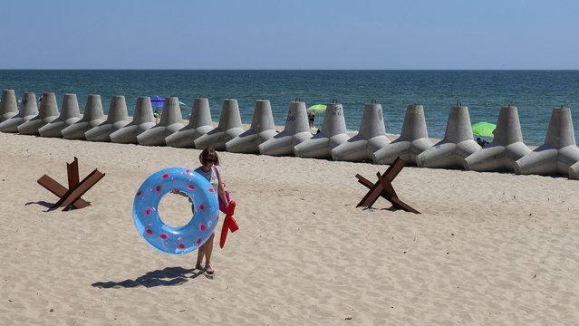 A person carries a swimming ring near tetrapods used as barriers against Russian military landing ships, amid Russia's attack on Ukraine, on the beach in the city of Chornomorsk, Odesa region, Ukraine on July 9, 2024. (Photo by Nina Liashonok/Reuters)