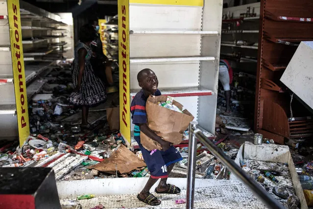 A young boy reacts as he collects food and drinks from a burnt down and looted Auchan supermarket in the up-market area of Almadies in Dakar on March 6, 2021 as protests have been ongoing for three days in Senegal after opposition leader Ousmane Sonko was arrested following rape charges. The Senegal government vowed on March 5, 2021 to use “all means necessary” to return order after police fired tear gas in clashes with supporters of opposition leader Ousmane Sonko as the Interior Minister said four people had died. (Photo by John Wessels/AFP Photo)
