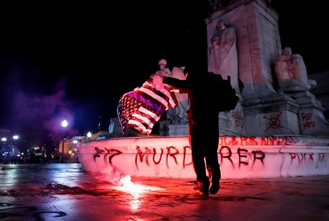 A fire is seen as a protester holds a thin blue line flag at the Christopher Columbus Memorial Fountain during a demonstration in Washington, D.C. to protest police violence, after the death of Daunte Wright, who was shot and killed by a police officer in Minnesota, U.S., April 17, 2021. (Photo by Erin Scott/Reuters)