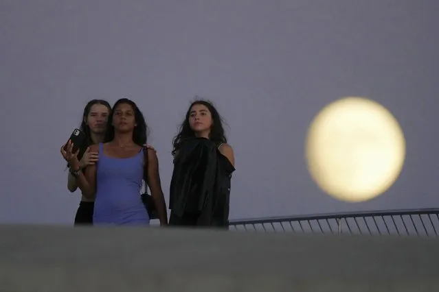 Girls stand on the roof of Lisbon's Museum of Art, Architecture and Technology as a nearly full moon rises in the background, Tuesday, Aug. 29, 2023. August 30 will see the month's second supermoon, when a full moon appears a little bigger and brighter thanks to its slightly closer position to Earth. (AP Photo/Armando Franca)