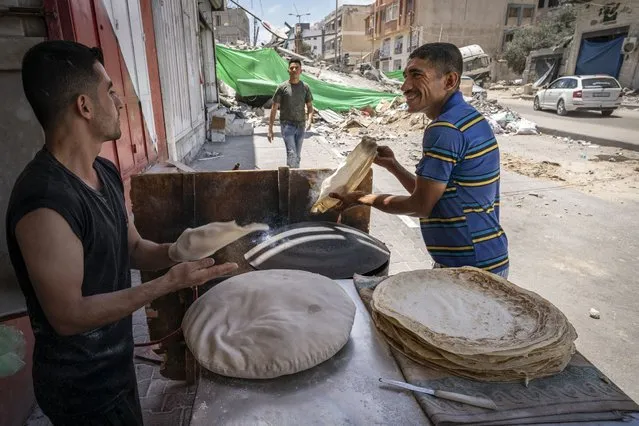 Bakery workers smile as they produce flatbreads at roadside near the debris pile of a building destroyed by an airstrike prior to a cease-fire reached after an 11-day war between Gaza's Hamas rulers and Israel, in Gaza City, Saturday, May 22, 2021. (Photo by John Minchillo/AP Photo)