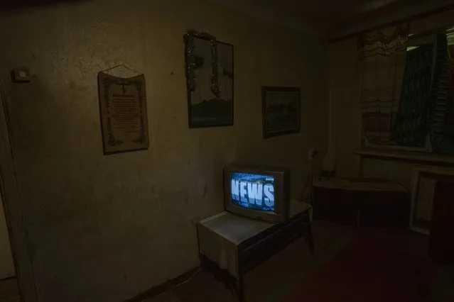 Seventy-year-old pensioner Valerii Ilchenko, who lives alone and is refusing to evacuate, watches the news on his tv in his apartment, in Kramatorsk, eastern Ukraine, Wednesday, July 6, 2022. Now a widower, Ilchenko says he still has no intention of leaving. “I don't have anywhere to go and don't want to either. What would I do there? Here at least I can sit on the bench, I can watch TV”, he says in an interview in his single-room apartment. (Photo by Nariman El-Mofty/AP Photo)