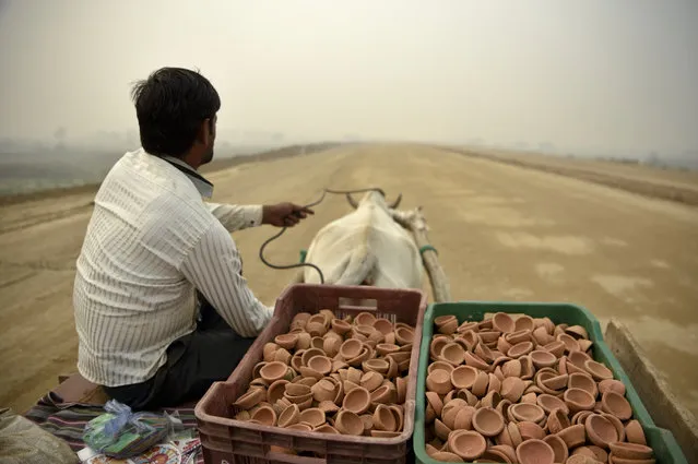 A man selling traditional earthen lamps ahead of Diwali festival, rides a bullock cart through an under construction road on a foggy day in Greater Noida, near New Delhi, India, Monday, November 5, 2018. With air quality reduced to “very severe” in the Indian capital region, authorities are bracing for a major Hindu festival featuring massive fireworks that threatens to cloak New Delhi with more toxic smog and dust. (Photo by R.S. Iyer/AP Photo)
