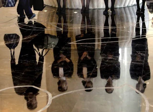 A porter carries luggage past a group of reception staff that are reflected in the floor as they stand in the foyer of the five-star rated Sofitel Hotel in Beijing in this November 19, 2007 file photo. (Photo by David Gray/Reuters)