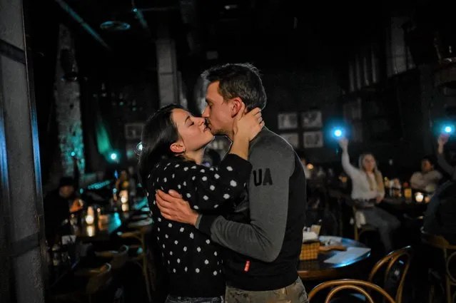 A couple kisses in a bar as clients put up lights during a power cut in Kyiv on November 24, 2022, amid the Russian invasion of Ukraine. (Photo by Bulent Kilic/AFP Photo)