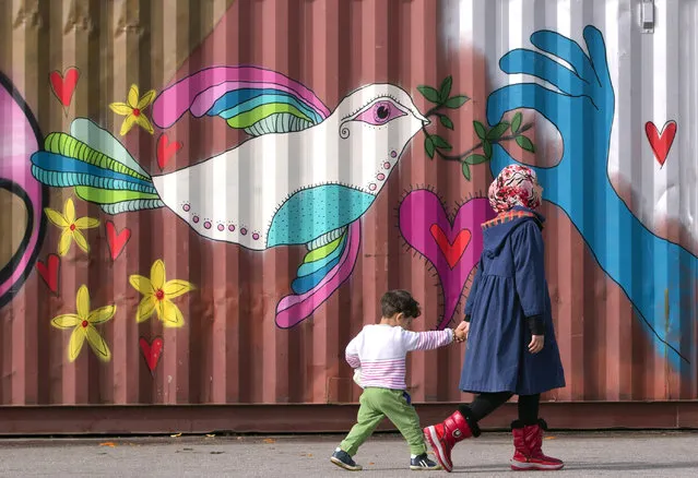 Children walk by a painted container as people wait in line for food handouts outside an overcrowded shelter area for migrants at the Athens' port of Piraeus, Tuesday, March 1, 2016. (Photo by Vadim Ghirda/AP Photo)