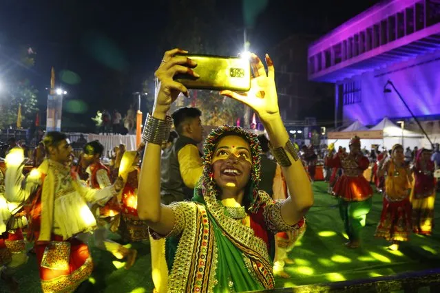 An Indian girl wearing traditional attire takes selfie as others perform the Garba, a dance of Gujarat state, to celebrate the Hindu festival Navratri in Ahmedabad, India, Thursday, October 7, 2021. Navratri, or nine nights festival, began Thursday. (Photo by Ajit Solanki/AP Photo)