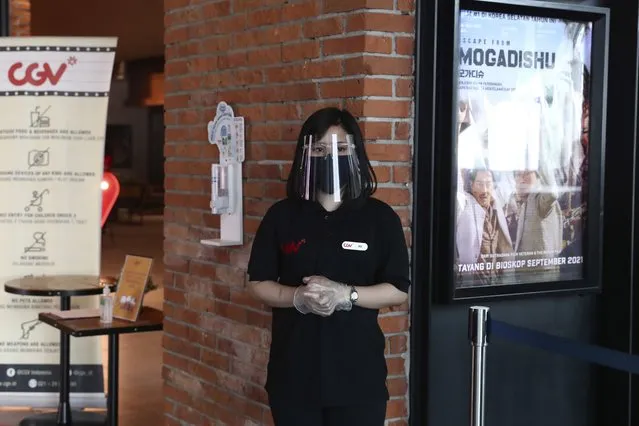 An employee wearing protective equipments to prevent the spread of coronavirus waits for customers during the first day of reopening at a cinema in Jakarta, Indonesia, Thursday, September 16, 2021. Cinemas in several cities shut during the deadly wave of coronavirus outbreak that hit the country in July were allowed to begin reopening with capacity limit as cases decline. (Photo by Tatan Syuflana/AP Photo)