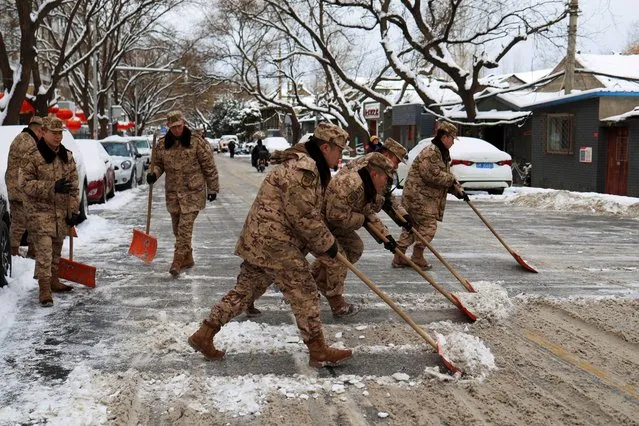 Paramilitary police officers remove snow from a road following snowfall in Beijing, China on February 21, 2024. (Photo by Florence Lo/Reuters)