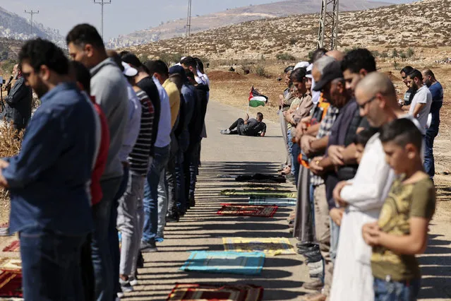 A Palestinian protester waves a national flag, as others proform the Friday prayers during a demonstration against the establishment of Israeli outposts on their lands, in Beit Dajan, east of Nablus in the Israeli-occupied West Bank, on October 22, 2021. (Photo by Abbas Momani/AFP Photo)