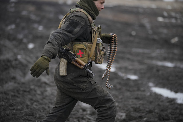 A Ukrainian serviceman runs to deliver ammunition to an armored fighting vehicle during a live fire exercise in a Joint Forces Operation controlled area in the Donetsk region, eastern Ukraine, Thursday, February 10, 2022. A peace agreement for the separatist conflict in eastern Ukraine that has never quite ended is back in the spotlight amid a Russian military buildup near the country's borders and rising tensions about whether Moscow will invade. (Photo by Vadim Ghirda/AP Photo)