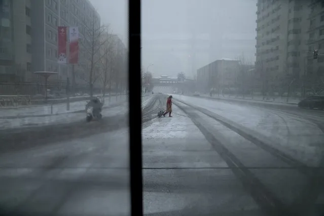 A woman crosses a street, seen from a window bus, at the 2022 Winter Olympics, Sunday, February 13, 2022, in Beijing. (Photo by Natacha Pisarenko/AP Photo)