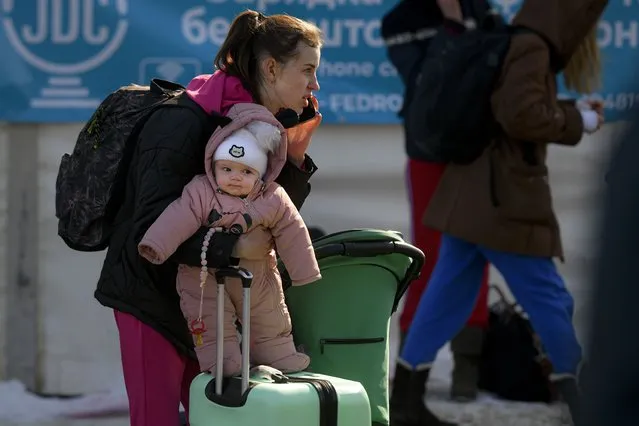 A refugee fleeing the conflict from neighbouring Ukraine tries to balance a baby and talk on the phone after crossing the border, at the Romanian-Ukrainian border, in Siret, Romania, Wednesday, March 9, 2022. (Photo by Andreea Alexandru/AP Photo)