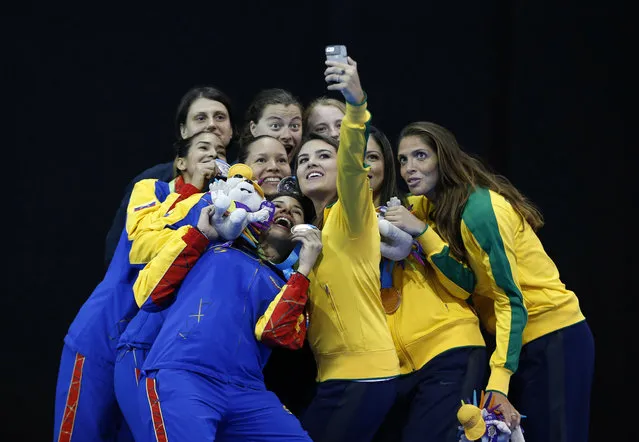 Medalists in the women's epee team fencing competition pose together for a selfie on the medals podium at the Pan Am Games in Toronto, Friday, July 24, 2015. Included are U.S. gold medalists Katharine Holmes, Katarzyna Trzopek, and Anna Catherine Van Brummen; Venezuelan silver medalists Eliana Lugo, Dayana Martinez, and Maria Martinez; and Brazilian bronze medalists Rayssa Costa, Nathalie Moellhausen, and Amanda Simeao. (Photo by Rebecca Blackwell/AP Photo)