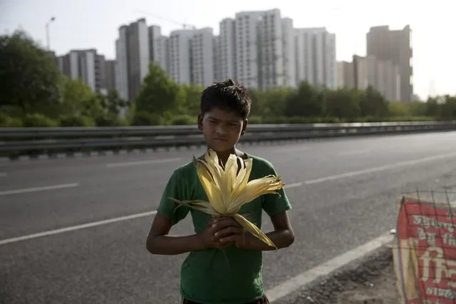 In this Tuesday, June 6, 2017 photo, Vikas, 12, an Indian boy who sells cooked corn along a busy expressway poses for a photo in Noida, India. (Photo by Tsering Topgyal/AP Photo)