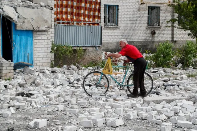 A man pushes a bicycle near a residential building destroyed during Ukraine-Russia conflict in the town of Rubizhne in the Luhansk region, Ukraine on June 1, 2022. (Photo by Alexander Ermochenko/Reuters)