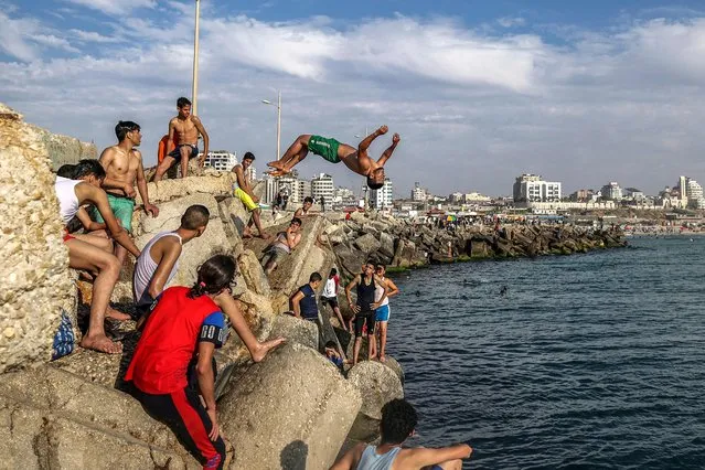 Youths watch as one performs a backflip while diving off rocks into the Mediterranean sea in Gaza City on May 20, 2022. (Photo by Mahmud Hams/AFP Photo)