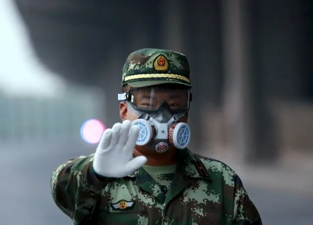 A paramilitary policeman wearing a mask gestures to the photographer to stop as he blocks a road leading to the evacuated residential area and explosion site, at Binhai new district in Tianjin, China, August 17, 2015. (Photo by Kim Kyung-Hoon/Reuters)