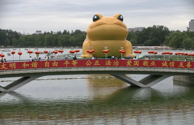 A giant inflatable “Golden Toad” is displayed on a lake as visitors cross a bridge at the Yu Yuan Tan Park in Beijing, China 21 July 2014. The installation designed by Chinese artist Guo Yong Rao measures 22 meters high, 34 meters long and 21 meters wide, and reminds many visitors of a golden toad that is a common symbol of good fortune and prosperity in Chinese culture. (Photo by Rolex Dela Pena/EPA)
