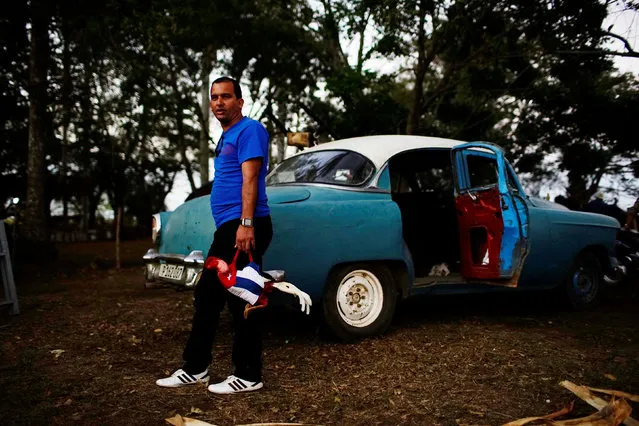 A cockfighting enthusiast stands beside a vintage car at a cockfighting arena on the outskirts of Santa Barbara, central region of Ciego de Avila province, Cuba, February 12, 2017. (Photo by Alexandre Meneghini/Reuters)