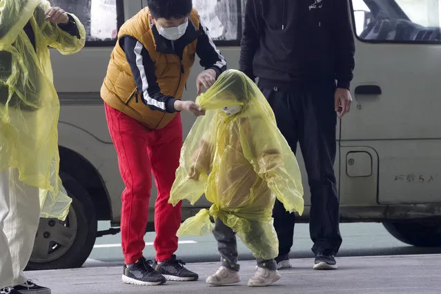 A woman wearing a face mask to protect against the spread of coronavirus puts a poncho on a child at Wuhan Tianhe International Airport in Wuhan in central China's Hubei Province, Wednesday, April 8, 2020. Within hours of China lifting an 11-week lockdown on the central city of Wuhan early Wednesday, tens of thousands people had left the city by train and plane alone, according to local media reports. (Photo by Ng Han Guan/AP Photo)
