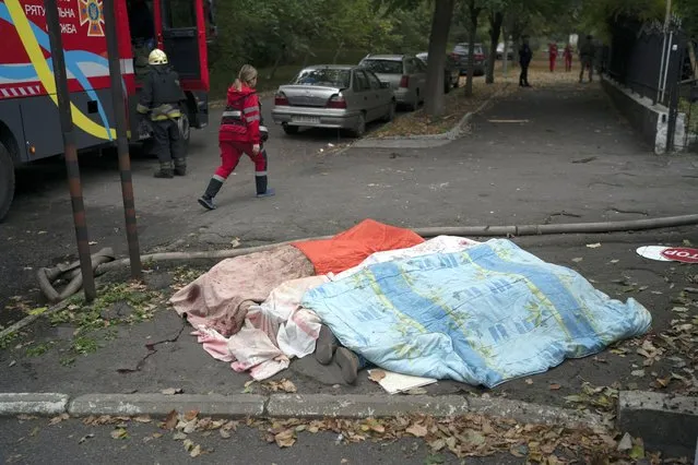 A member of the rescue service walks past three bodies, covered by blankets, following a Russian attack in Dnipro, Ukraine, Monday, October 10, 2022. Explosions on Monday rocked multiple cities across Ukraine, including missile strikes on the capital Kyiv for the first time in months. (Photo by Leo Correa/AP Photo)