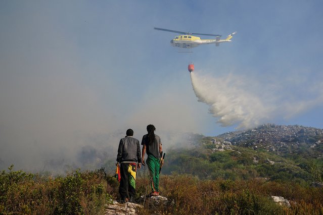 Residents look on at a helicopter helping to extinguish a fire in the mountains around Ocean View, Cape Town, South Africa on January 22, 2024. (Photo by Nic Bothma/Reuters)