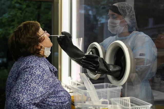 A staff member of AltraVita fertility clinic takes a swab from an outdoor booth as a woman undergoes a test for the coronavirus disease (COVID-19) in Moscow, Russia on June 10, 2020. The clinic added coronavirus testing to its list of services and installed a booth outdoors so clients can safely get tested for the disease. (Photo by Evgenia Novozhenina/Reuters)