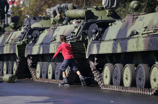 A boy practices roller skating pasts Serbian army armored personal carriers placed in Usce park, seven days before an upcoming military parade, in Belgrade, Serbia, Thursday, October 9, 2014. The military parade scheduled for October 16, marks the 70th anniversary of the liberation of Belgrade in the Second World War. Russian President Vladimir Putin will be attending the ceremony. (Photo by Darko Vojinovic/AP Photo)