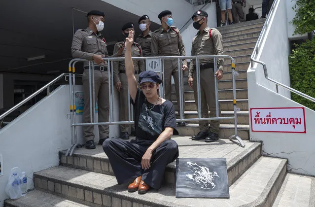 A pro-democracy supporter raises a three-finger salute, a symbol of resistance, in front of police officers at the Samranrat police station in Bangkok, Thailand, Thursday, August 20, 2020. Thai police arrested a rapper and four pro-democracy activists in a crackdown on growing protests that have emerged as the most serious threat to the government led by a former army general they accuse of incompetence and corruption. (Photo by Sakchai Lalit/AP Photo)