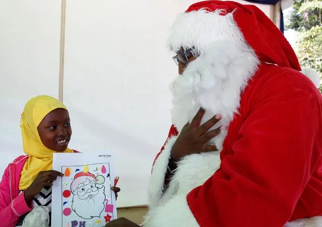 A Muslim child shows a picture of Santa Clause to Victor Njoroge, dressed in a Santa Claus costume, during a children's Christmas festival at the Junction Shopping Mall ahead of Christmas, in Nairobi, Kenya on December 17, 2022. (Photo by Monicah Mwangi/Reuters)