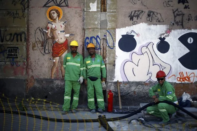 Workers stand in front of a graffitti in Rio de Janeiro, Brazil August 2, 2016. (Photo by Ivan Alvarado/Reuters)