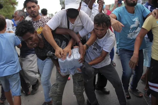 Migrants scuffle to take bottles of water during a distribution by local authorities near Mytilene town, on the northeastern island of Lesbos, Greece, Saturday, September 12, 2020. Thousands of asylum-seekers spent a fourth night sleeping in the open on the Greek island of Lesbos, after successive fires destroyed the notoriously overcrowded Moria camp during a coronavirus lockdown. (Photo by Petros Giannakouris/AP Photo)