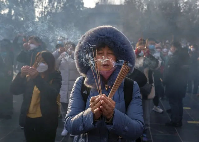 A woman holds incense sticks as people perform prayers for good fortune at Yonghegong, or the Lama Temple, for the Chinese Lunar New Year on January 22, 2023 in Beijing, China. The prayers were the first Lunar New Year prayers without restrictions since the pandemic began in 2020, after the Chinese government changed its strict zero Covid policy last month.  (Photo by Kevin Frayer/Getty Images)
