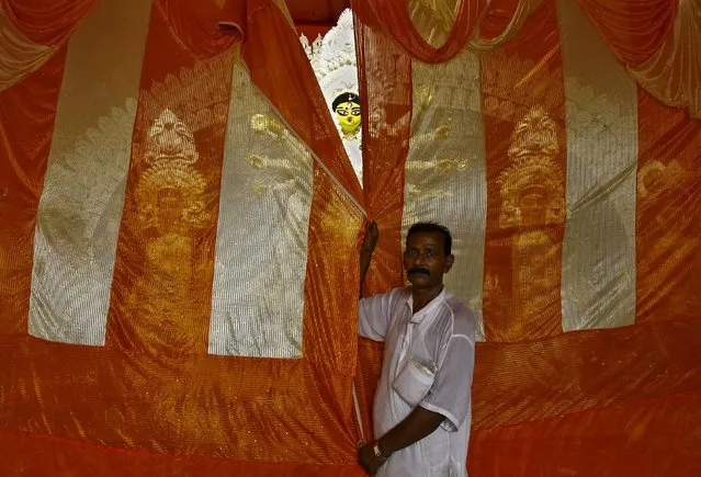 A devotee covers the idol of Hindu goddess Durga as a priest (behind curtain) offers bhog (offerings made to the goddess Durga which is later distributed among the devotees) at a pandal or temporary platform during the religious festival of Durga Puja in Kolkata, India, October 21, 2015. (Photo by Rupak De Chowdhuri/Reuters)