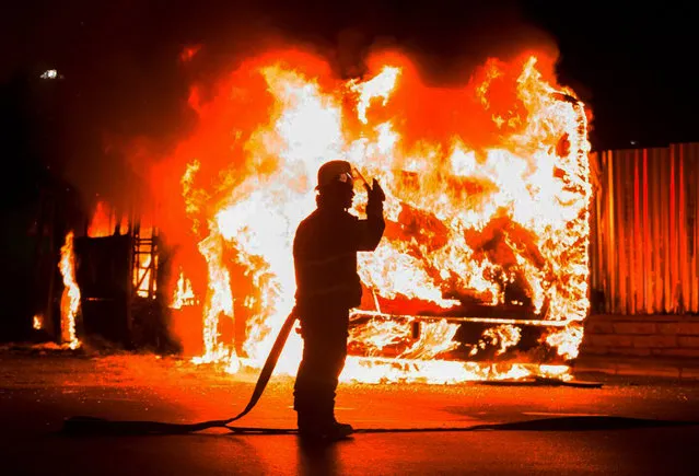 A fireman stands at a burning bus in Braamfontein, Johannesburg, South Africa, Tuesday, October 25, 2016. (Photo by Yeshiel Panchia/AP Photo)