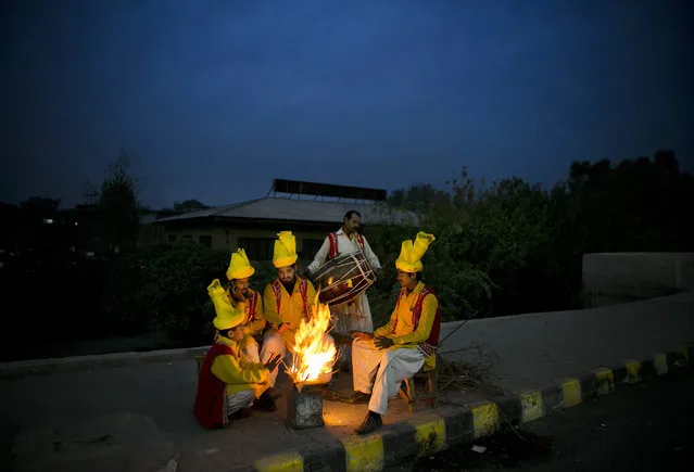 Pakistani street performers sit around fire waiting for customers on a chilly evening in Rawalpindi, Pakistan, Wednesday, November 11, 2015. Some parts of Pakistan are facing a harsh winter. (Photo by B.K. Bangash/AP Photo)