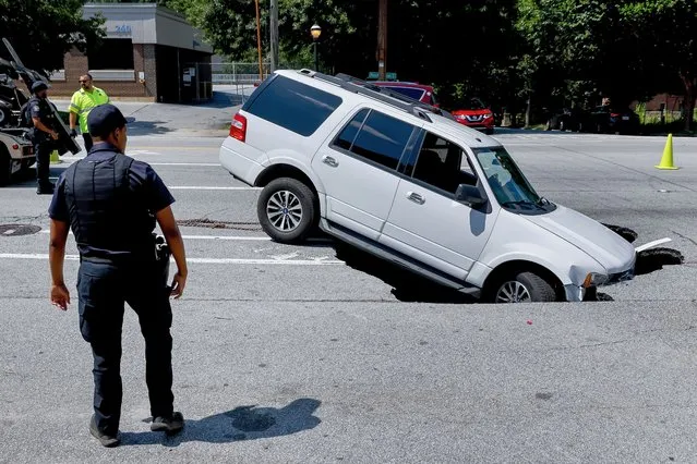 An Atlanta Police Department officer investigates the scene after an SUV was partially swallowed by a sinkhole along the busy Ponce de Leon Avenue in midtown Atlanta, Georgia, USA, 27 June 2023. Officials have not released why the sinkhole opened up along the roadway, closing at least two lanes of traffic. (Photo by Erik S. Lesser/EPA)