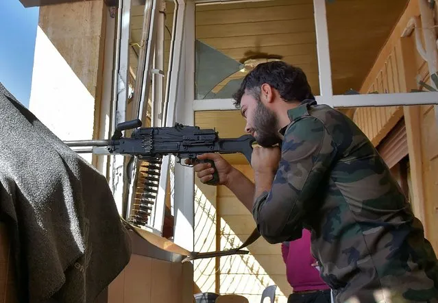 A Syrian pro-government fighter looks on from his sniper nest in a building in Aleppo's western Minyan district on November 10, 2016. The Observatory said that regime forces earlier in the week had retook the Minyan district in the west from rebels. Aleppo has been divided between government control in the west and rebel control in the east since mid-2012, but in recent months regime troops have surrounded the east, laying siege to it. (Photo by George Ourfalian/AFP Photo)