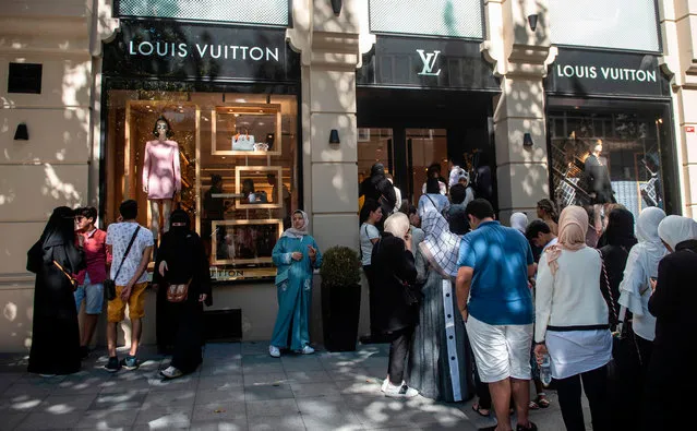 Tourists, many from Saudi Arabia and Asia, queue outside a luxury brand Louis Vuitton store in Istanbul on August 13, 2018. The collapse of the Turkish lira has caused trauma as Turks see their purchasing power reduced but has been an unexpected windfall for foreign tourists visiting the country at the peak of the summer season. Tourists, mainly from Saudi Arabia and Asia, formed long queues outside luxury brand design stores like Louis Vuitton, Chanel and Prada when the Turkish currency took a severe hit against dollar, falling over 16 percent on its value on August 10. (Photo by Yasin Akgul/AFP Photo)