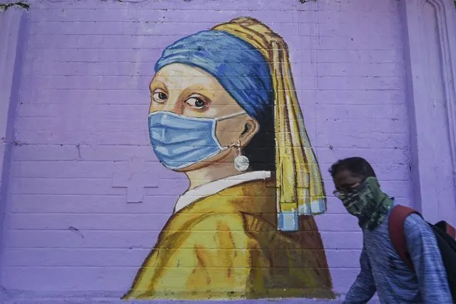 A pedestrian walks past a mural of Johannes Vermeer's “Girl with a Pearl Earring” wearing a facemask to spread awareness about the COVID-19 coronavirus, in Mumbai on March 31, 2021. (Photo by Indranil Mukherjee/AFP Photo)