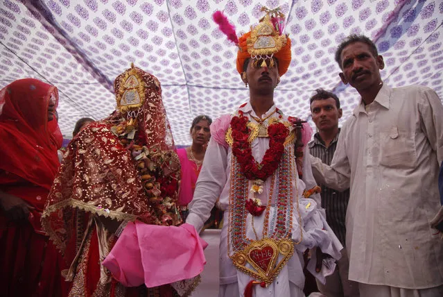 An Indian bride and groom in traditional attire perform wedding rituals during a mass marriage of thirty five couple belonging to Rajasthan's Sargara community in Ahmadabad, Gujarat state, India, Sunday, January 24, 2016.Mass marriages in India are organized by social organizations primarily to help the economically backward families who cannot afford the high ceremony costs as well as the customary dowry and expensive gifts that are still prevalent in many communities. (Photo by Ajit Solanki/AP Photo)