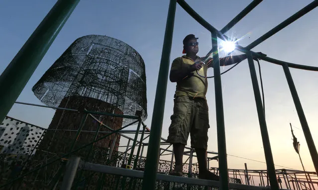 In this Thursday, December 15, 2016 photo, a Sri Lankan port worker welds steel frames to assemble an enormous, artificial Christmas tree on a popular beachside promenade in Colombo, Sri Lanka. Hundreds of Sri Lanka’s port workers and volunteers are struggling to put up the towering Christmas tree in time for the holidays. The majority-Buddhist nation is aiming to beat the world record for the tallest, artificial Christmas tree as a show of multicultural respect. But twice the construction deadline was missed, and now organizers hope to erect the tree on Christmas Eve. The Catholic Church has criticized the $80,000 price tag as a waste of money that is better spent helping the poor. (Photo by Eranga Jayawardena/AP Photo)