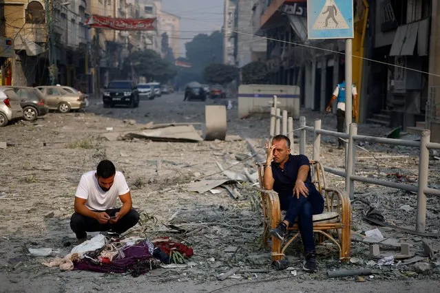 Palestinians sit on a debris-strewn street near the Watan Tower, which was destroyed in Israeli strikes, in Gaza City on October 8, 2023. (Photo by Mohammed Salem/Reuters)