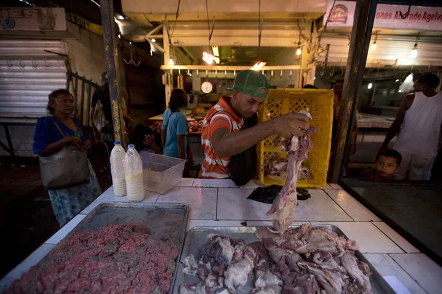 In this August 19, 2018 photo, butcher Johel Prieto places spoiled meat on a tray to sell at the central market in Maracaibo, Venezuela. Prieto said the ongoing power outages turned an entire side of beef rotten in his shop. Determined to turn a profit, he ground up the putrid bits and mixed them with a little fresh red meat. (Photo by Fernando Llano/AP Photo)