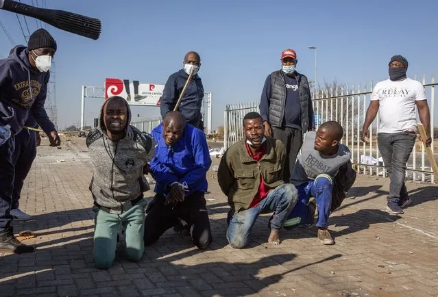 Young men are punished by members of a taxi association, after they were caught while making off with goods from a store in Vosloorus, Johannesburg, Wednesday, July 14, 2021. (Photo by Yeshiel Panchia/AP Photo)