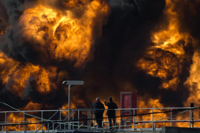 Workers watch fire fighters fight flames in a fuel tank in Oil Refineries Ltd in Haifa bay, Israel, Sunday, December 25, 2016. Oil Refineries Ltd. located in the bay area of Haifa, is Israel's largest Oil refinery. (Photo by Ariel Schalit/AP Photo)