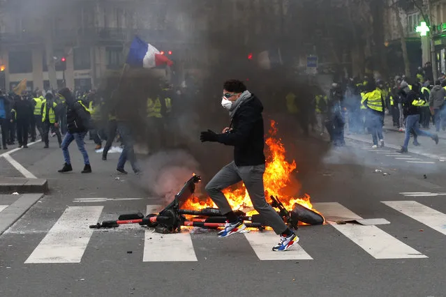 A demonstrator runs by a fire during a yellow vest protest Saturday, February 2, 2019 in Paris. France's yellow vest protesters are taking to the streets to keep pressure on French President Emmanuel Macron's government, for the 12th straight weekend of demonstrations. This week, demonstrators in the French capital are planning to pay tribute to the yellow vests injured during clashes with police. (Photo by Francois Mori/AP Photo)