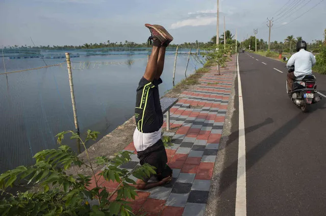 A man performs yoga in the morning by a roadside overlooking the backwaters in Kochi, Kerala state, India, Monday, September 20, 2021. (Photo by R.S. Iyer/AP Photo)